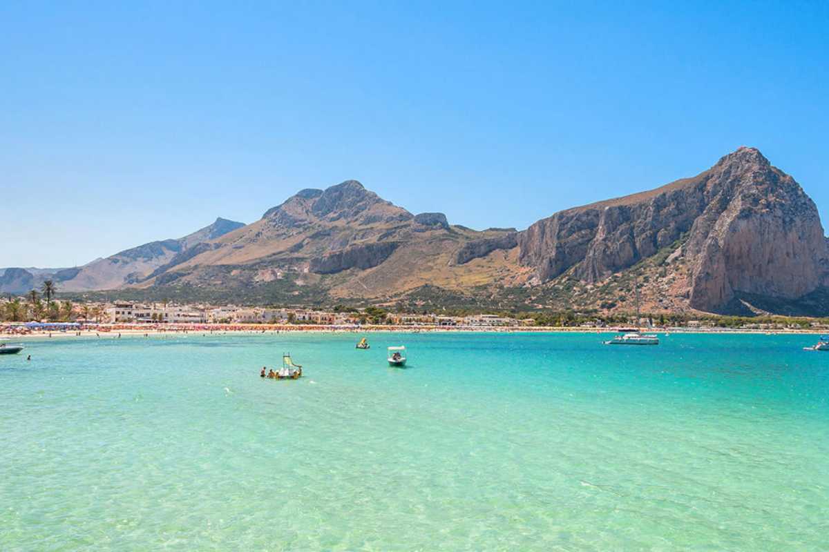 Dettaglio della facciata del Santuario di San Vito Martire, con pellegrini e turisti davanti, cielo terso e palme, atmosfera di festa