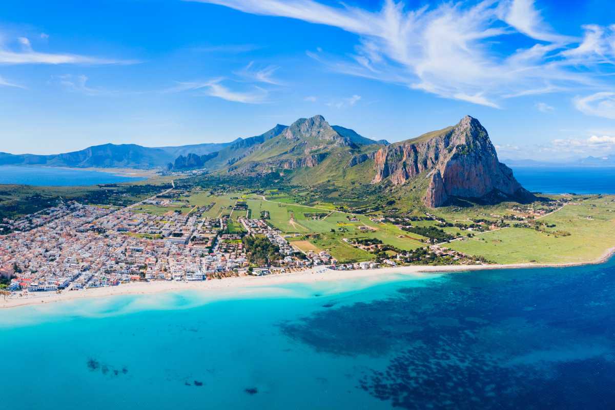 Scorcio panoramico della spiaggia di San Vito Lo Capo al tramonto, con Monte Monaco sullo sfondo, persone che passeggiano sulla sabbia e barche di pescatori in primo piano